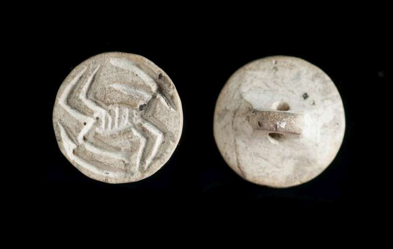קָמֵעַ-חותם מעוגל דמוי-כפתור ועליו שתי דמויות של אנטילופות במערך טֶט-בֶּשׁ (ראש-אל-זנב)