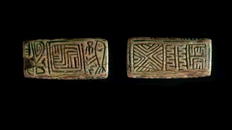 Design amulet depicting geometric motifs on both sides, with one side also depicting a bird